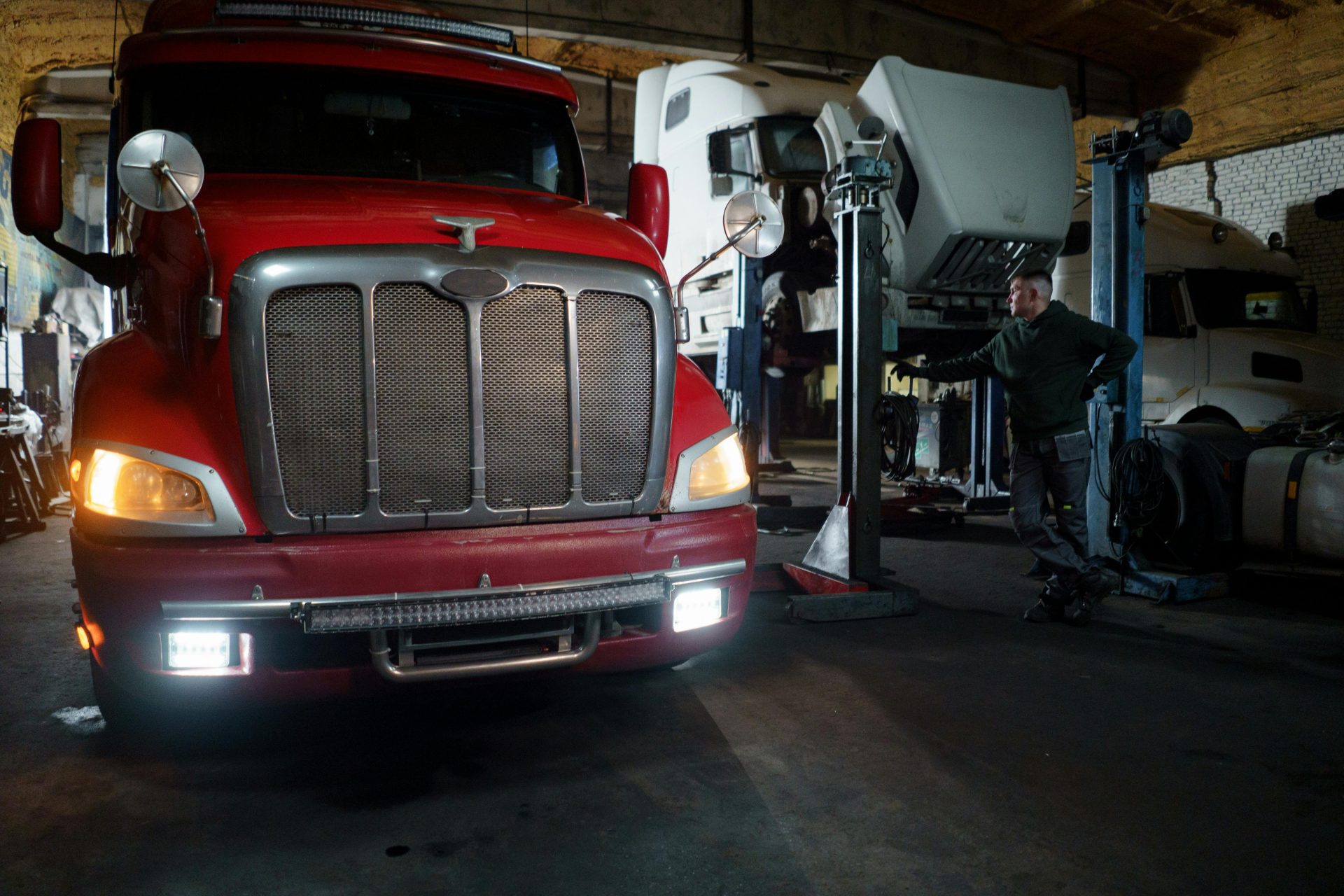 Red truck in a garage with mechanic and elevated vehicles undergoing maintenance.