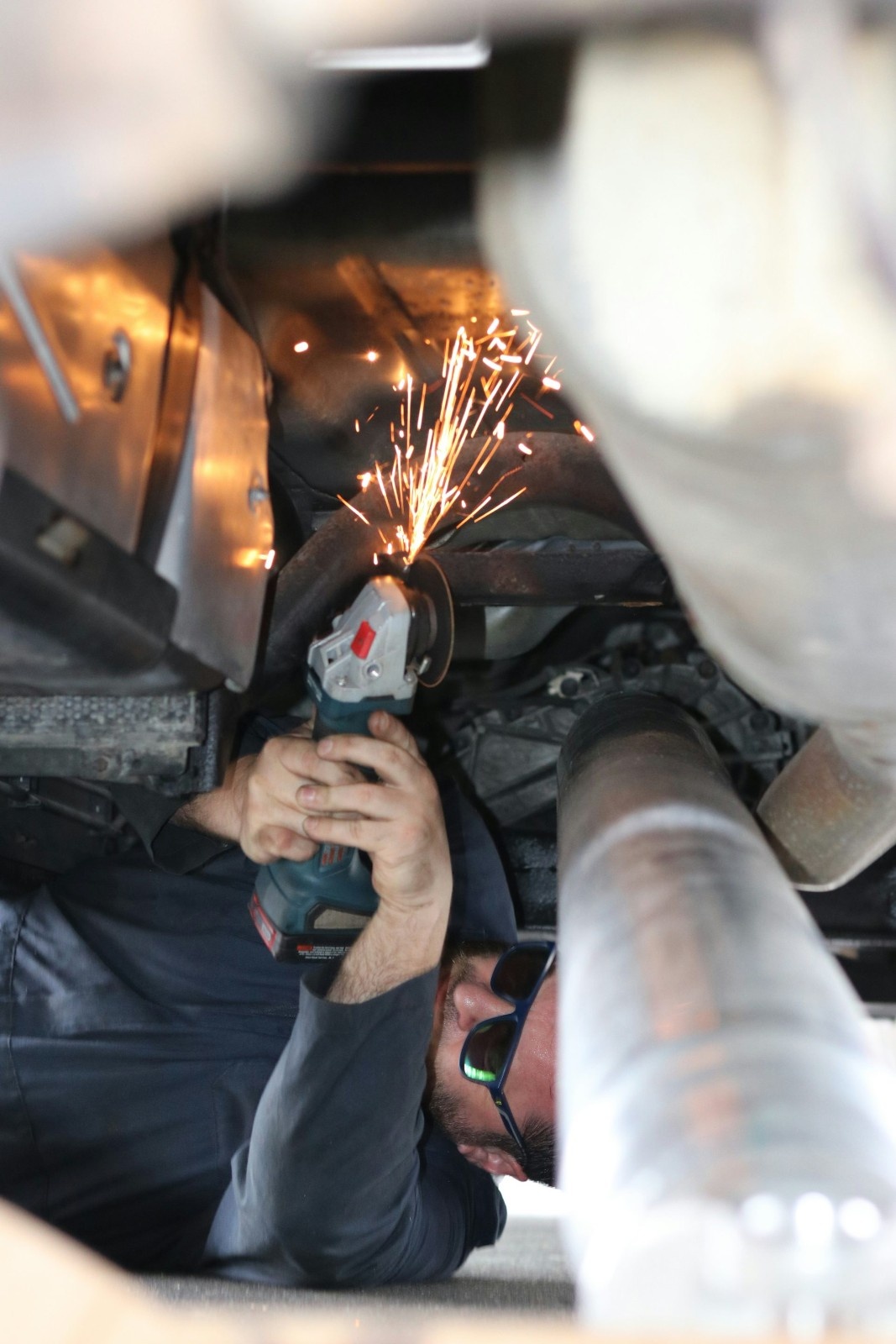 A mechanic uses a grinder under a car.